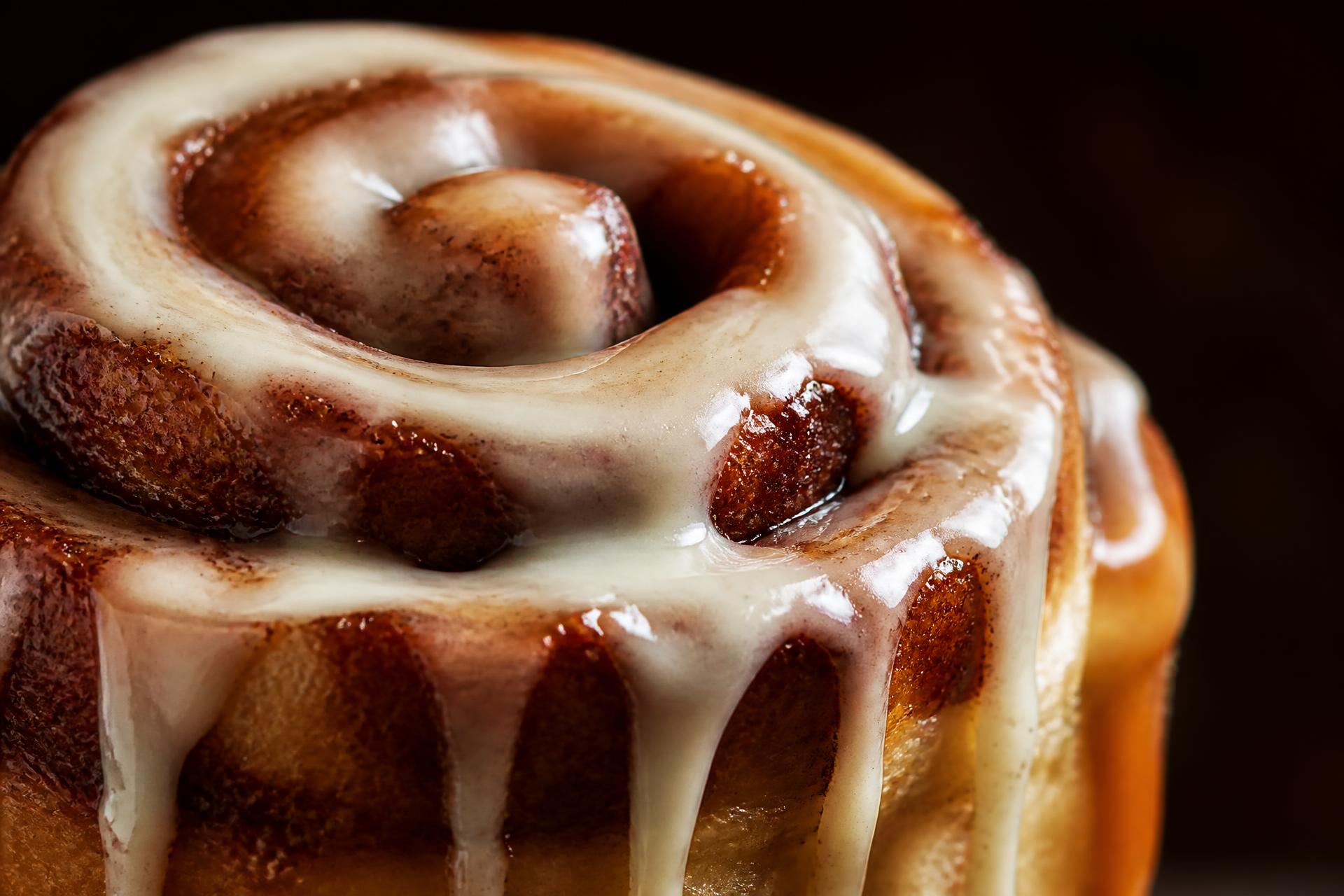 Close crop of a cinnamon roll with glaze dripping down its warm swirls